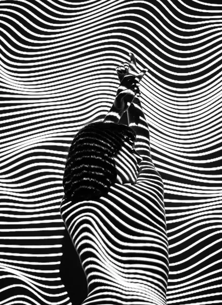 A black-and-white photograph of a figure against a rippling striped pattern, posted in its original proportions