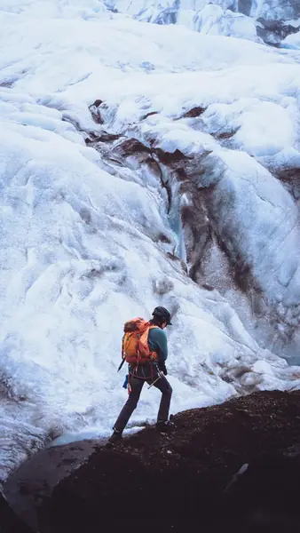 A hiker with an orange backpack on a glacier, cropped to a 9:16 vertical story