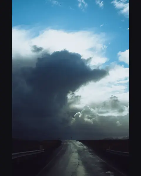 A wet road under a towering storm cloud, uncropped inside a 4:5 post on a near-black background
