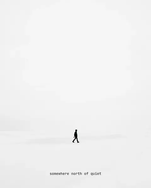A lone walker crossing an almost white snowfield, with the line “somewhere north of quiet” set very small beneath