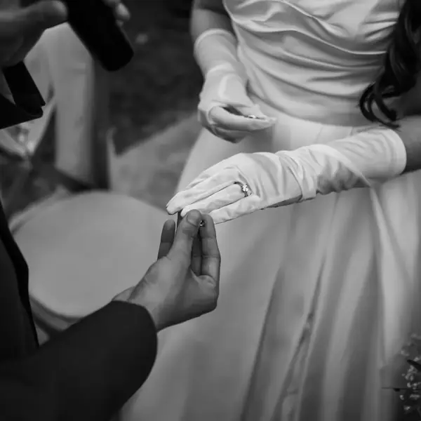 A black-and-white close view of a ring being placed on a gloved hand, cropped square