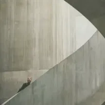 A tiny figure walking a concrete ramp, dwarfed by the curve of the wall